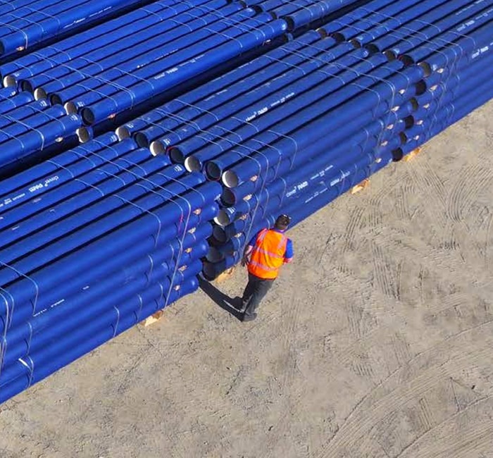 Man in high-vis vest standing next to stacks of ductile iron pipe.